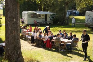 Foto der QFS-Mitarbeiterinnen und Mitarbeiter samt Familien beim Frühstück im Freien auf einem Zeltplatz